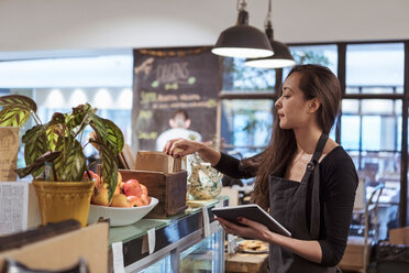 Junge Verkäuferin, die ein digitales Tablet hält, während sie in einem Café Waren analysiert - MASF10246
