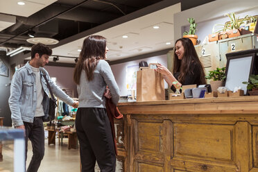 Smiling female cashier talking to customers at checkout counter - MASF10250