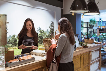 Saleswoman selling merchandise to female customer at checkout counter - MASF10255