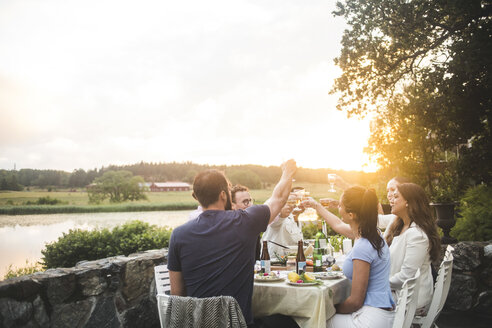 Männliche und weibliche Freunde stoßen mit Getränken am Esstisch gegen den Himmel bei Sonnenuntergang an - MASF10267