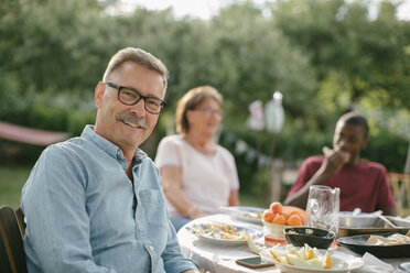 Porträt eines lächelnden älteren Mannes, der während einer Gartenparty mit seiner Familie am Tisch sitzt - MASF10268