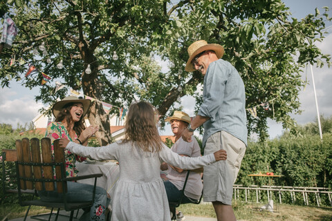 Family applauding while looking at senior man and girl dancing during garden party stock photo