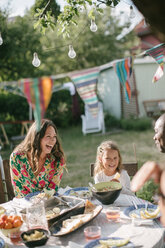 Glückliche Familie beim Mittagessen am Tisch im Hinterhof während einer Gartenparty - MASF10275