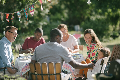 Glückliche Mehrgenerationenfamilie beim gemeinsamen Mittagessen im Garten während eines Gartenfestes, lizenzfreies Stockfoto