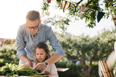 Grandfather teaching granddaughter to cut vegetable at table in backyard - MASF10286