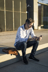 Mature man sitting in the city using cell phone - GIOF04900