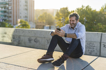 Smiling mature man sitting in the city using cell phone - GIOF04904