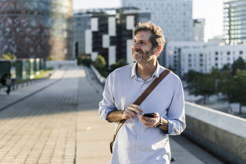 Lächelnder reifer Mann mit Mobiltelefon in der Stadt - GIOF04907