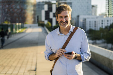 Porträt eines lächelnden reifen Mannes mit Mobiltelefon in der Stadt - GIOF04908
