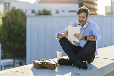 Mature man sitting in the city using tablet - GIOF04923