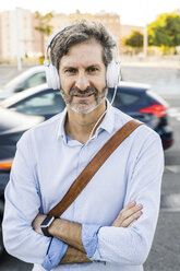 Porträt eines reifen Mannes mit Kopfhörern, der an einer Straße steht - GIOF04931