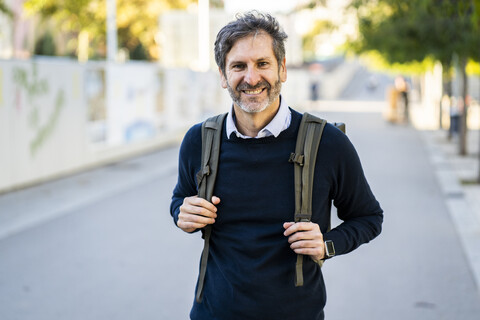 Portrait of smiling mature man wearing a backpack in the city stock photo