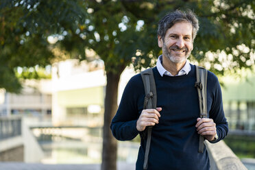 Portrait of smiling mature man wearing a backpack in the city - GIOF04938