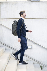 Lächelnder reifer Mann mit einem Rucksack, der eine Treppe in der Stadt hinuntergeht - GIOF04940