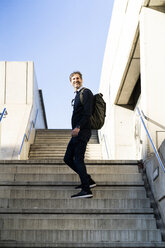 Lächelnder reifer Mann mit einem Rucksack auf einer Treppe in der Stadt - GIOF04941
