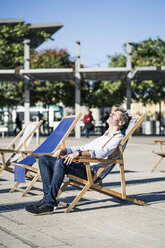 Mature man relaxing in deckchair on a square in the city - GIOF04947