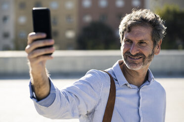 Lächelnder reifer Mann macht ein Selfie in der Stadt - GIOF04953