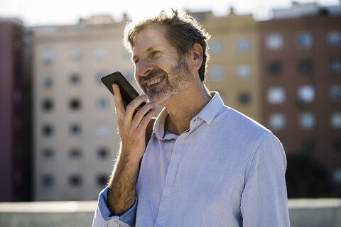 Lächelnder reifer Mann mit Handy in der Stadt, lizenzfreies Stockfoto