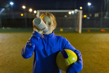 Girl soccer player taking a break, drinking water on field at night - HOXF04188