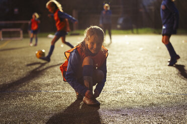 Portrait lächelnd Mädchen Fußballspieler binden Schuh auf dem Feld in der Nacht - HOXF04189
