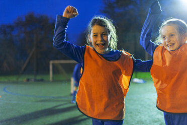 Portrait enthusiastic girl soccer players cheering on field at night - HOXF04190