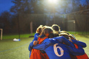 Girls soccer team huddling on field at night - HOXF04213