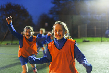 Portrait enthusiastic girl soccer players cheering on field at night - HOXF04225