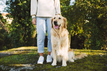 Frau neben Golden Retriever Hund auf einer Wiese sitzend - RAEF02229