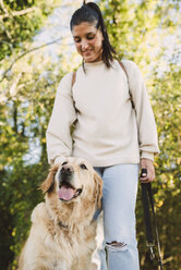 Lächelnde junge Frau mit ihrem Golden Retriever Hund in einem Park - RAEF02230