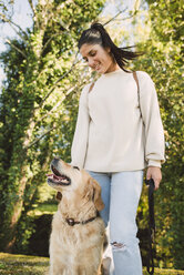 Lächelnde junge Frau mit ihrem Golden Retriever Hund in einem Park - RAEF02231