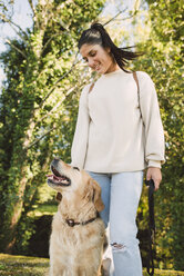 Smiling young woman with her Golden retriever dog in a park - RAEF02231