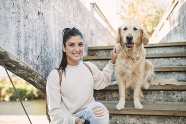 Porträt einer lächelnden jungen Frau mit ihrem Golden Retriever Hund auf einer Treppe im Freien - RAEF02234
