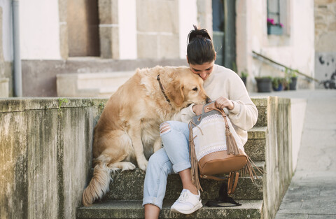 Young woman with her Golden retriever dog on stairs looking in backpack stock photo