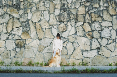 Junge Frau mit ihrem Golden Retriever Hund an einer Steinmauer - RAEF02240