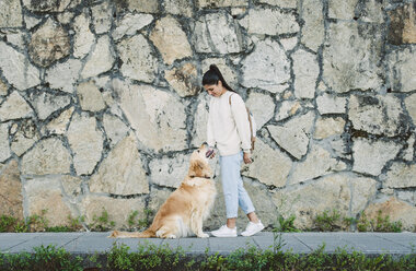 Young woman with her Golden retriever dog at a stone wall - RAEF02241