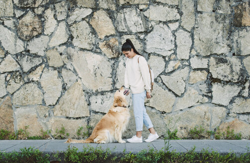 Junge Frau mit ihrem Golden Retriever Hund an einer Steinmauer - RAEF02241