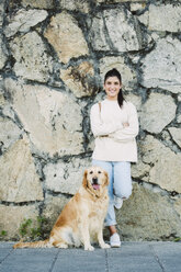 Portrait of a smiling young woman with her Golden retriever dog at a stone wall - RAEF02242