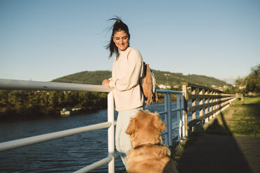 Lächelnde junge Frau, die ihren Hund am Wasser betrachtet - RAEF02244