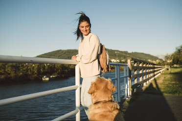 Smiling young woman looking at her dog at the waterfront - RAEF02244