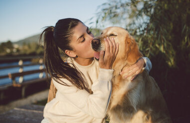 Junge Frau küsst ihren Golden Retriever Hund am Wasser - RAEF02247