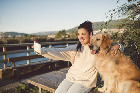 Lächelnde junge Frau macht ein Selfie mit ihrem Hund am Wasser - RAEF02248