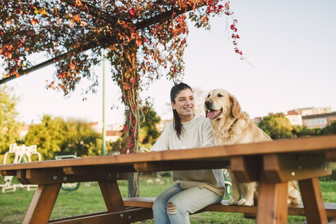 Lächelnde junge Frau mit ihrem Golden Retriever Hund, der sich in einem Park ausruht - RAEF02252