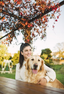 Lächelnde junge Frau mit ihrem Golden Retriever Hund, der sich in einem Park ausruht - RAEF02254