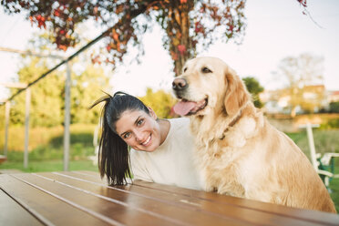 Porträt einer glücklichen jungen Frau mit ihrem Golden Retriever Hund, die sich in einem Park ausruhen - RAEF02256