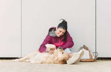 Happy young woman stroking and playing with her golden retriever dog - RAEF02262