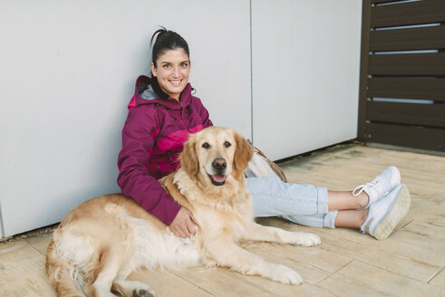 Porträt einer lächelnden jungen Frau mit ihrem Golden-Retriever-Hund, der an einer Wand sitzt - RAEF02263