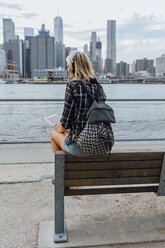 USA, New York City, Brooklyn, young woman sitting at the waterfront with backpack, headphones and tablet - BOYF01122