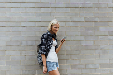 Junge Frau, die ihr Handy an einer Backsteinmauer überprüft - BOYF01124