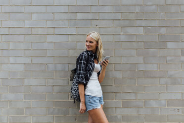 Smiling young woman with cell phone at brick wall - BOYF01125