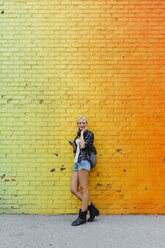 Porträt einer jungen Frau mit Mobiltelefon an einer bunten Backsteinmauer - BOYF01133